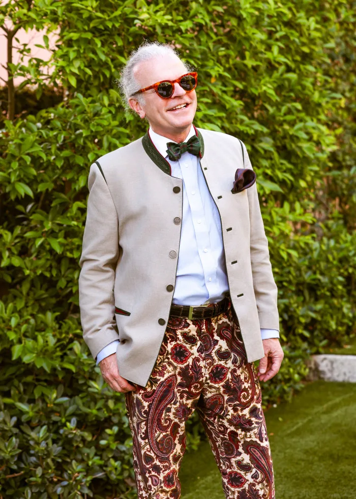 Timothy McVay in a tan jacket with green trim, a light blue shirt, a green bow tie, and paisley pants, smiling outdoors.
